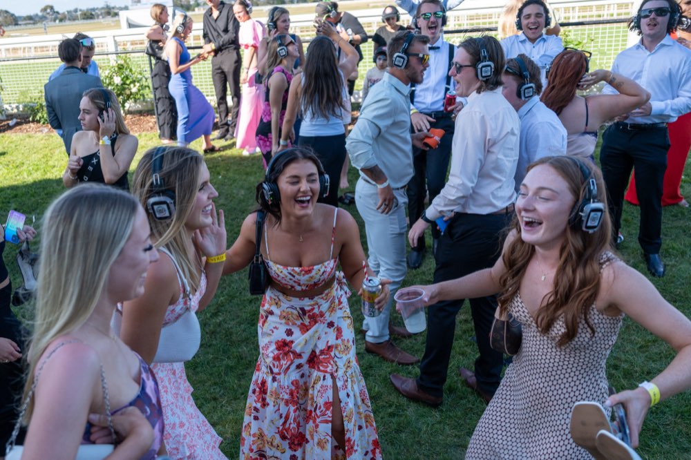 Guests at an outdoor Simple Entertainment silent disco laughing and dancing on the grass, wearing wireless LED headphones.
